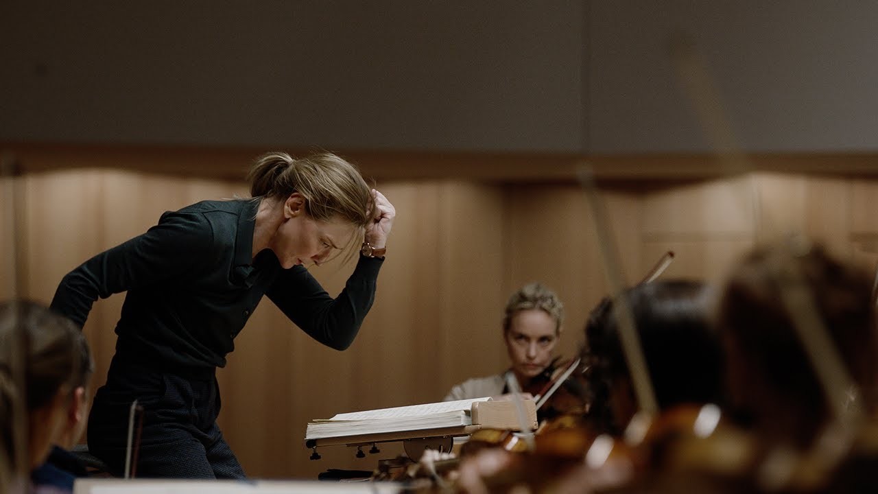 Actor Cate Blanchett is conducting in a rehearsal room. Her baton is up in the air but she is looking down over the musical score. 