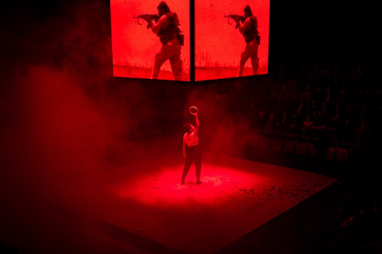 photo of Zahra Newman holding a crown above her head on an almost entirely red-lit stage