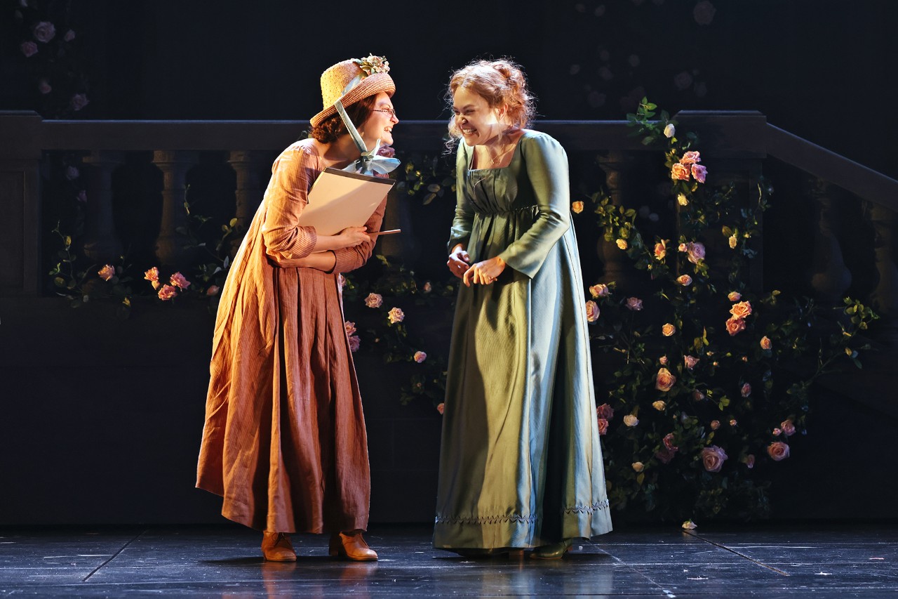 two women are standing and giggling, they wear bonnets