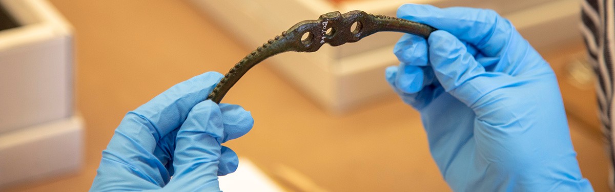 A pair of latex gloved hands handling a museum artefact.
