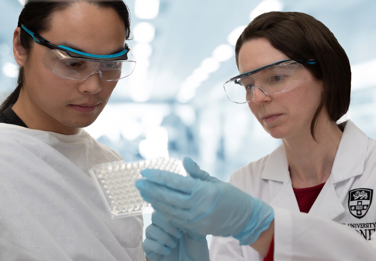 Two researchers in white lab coats holding vials.