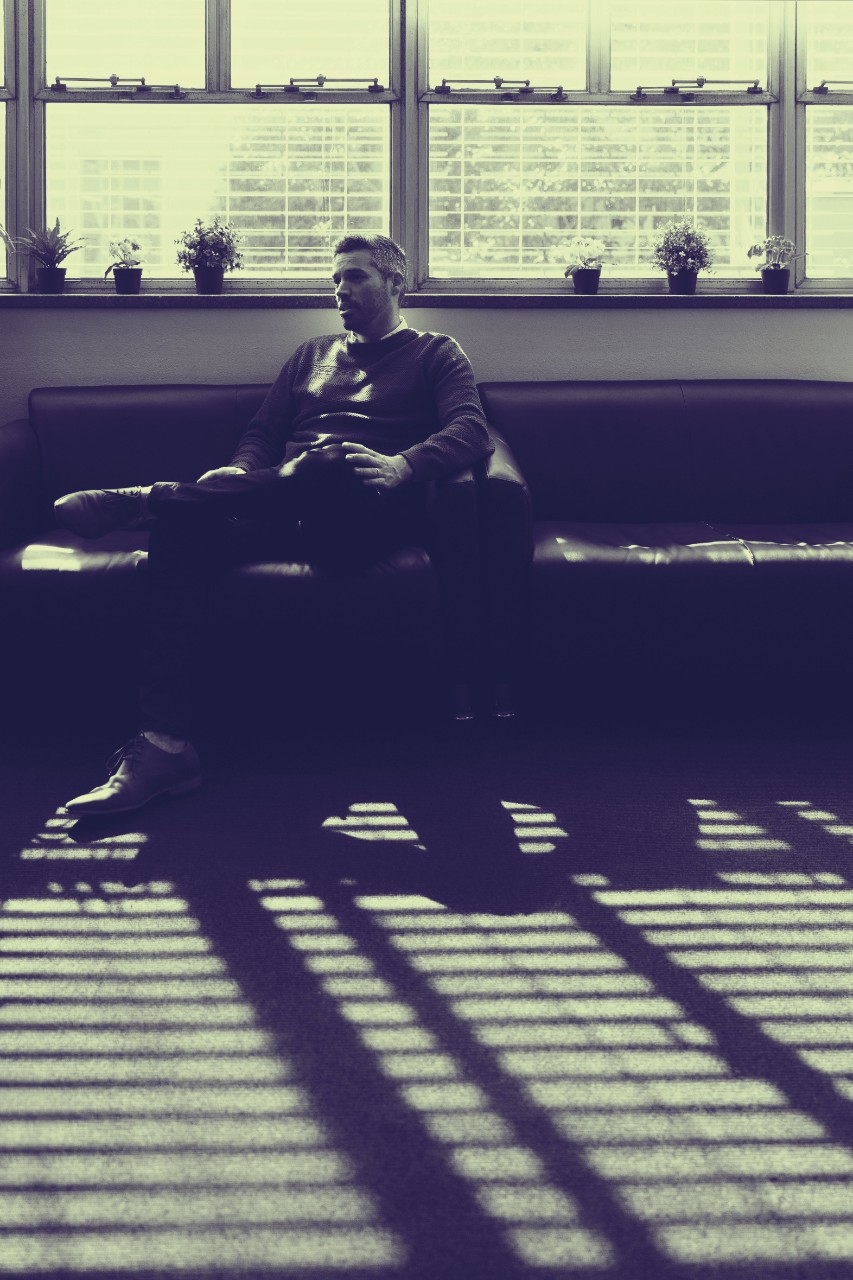Dr Ben Colagiuri sitting in his office amid dramatic shadows and light streaming through blinds