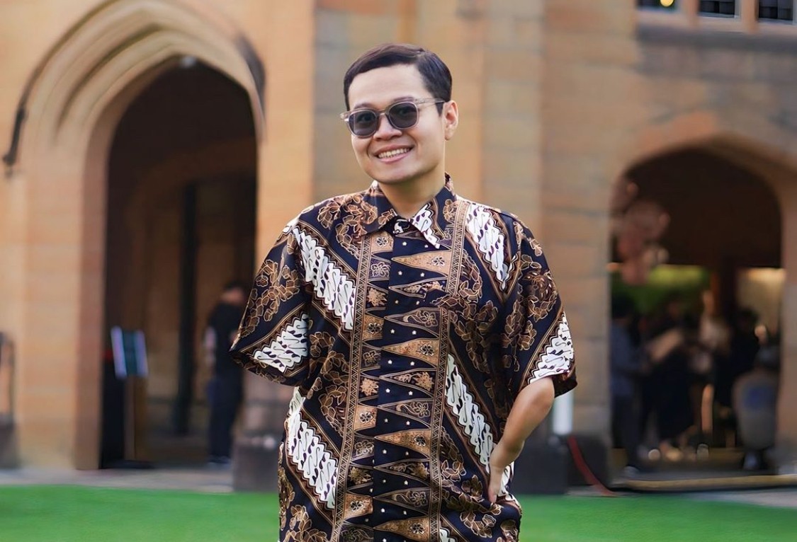 Umar, a young man in a Batik shirt, stands outside a sandstone building at the University of Sydney.