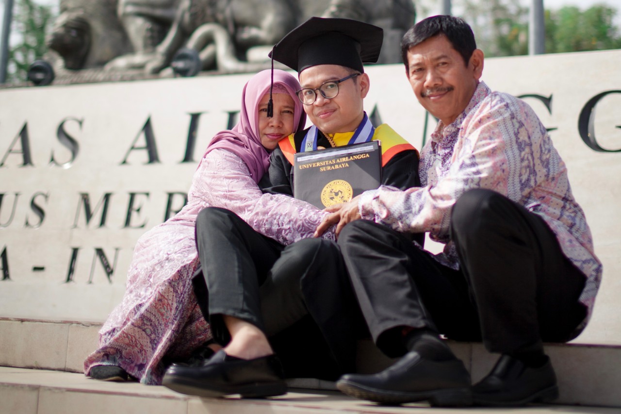 Umar in graduation robes sits between his parents.