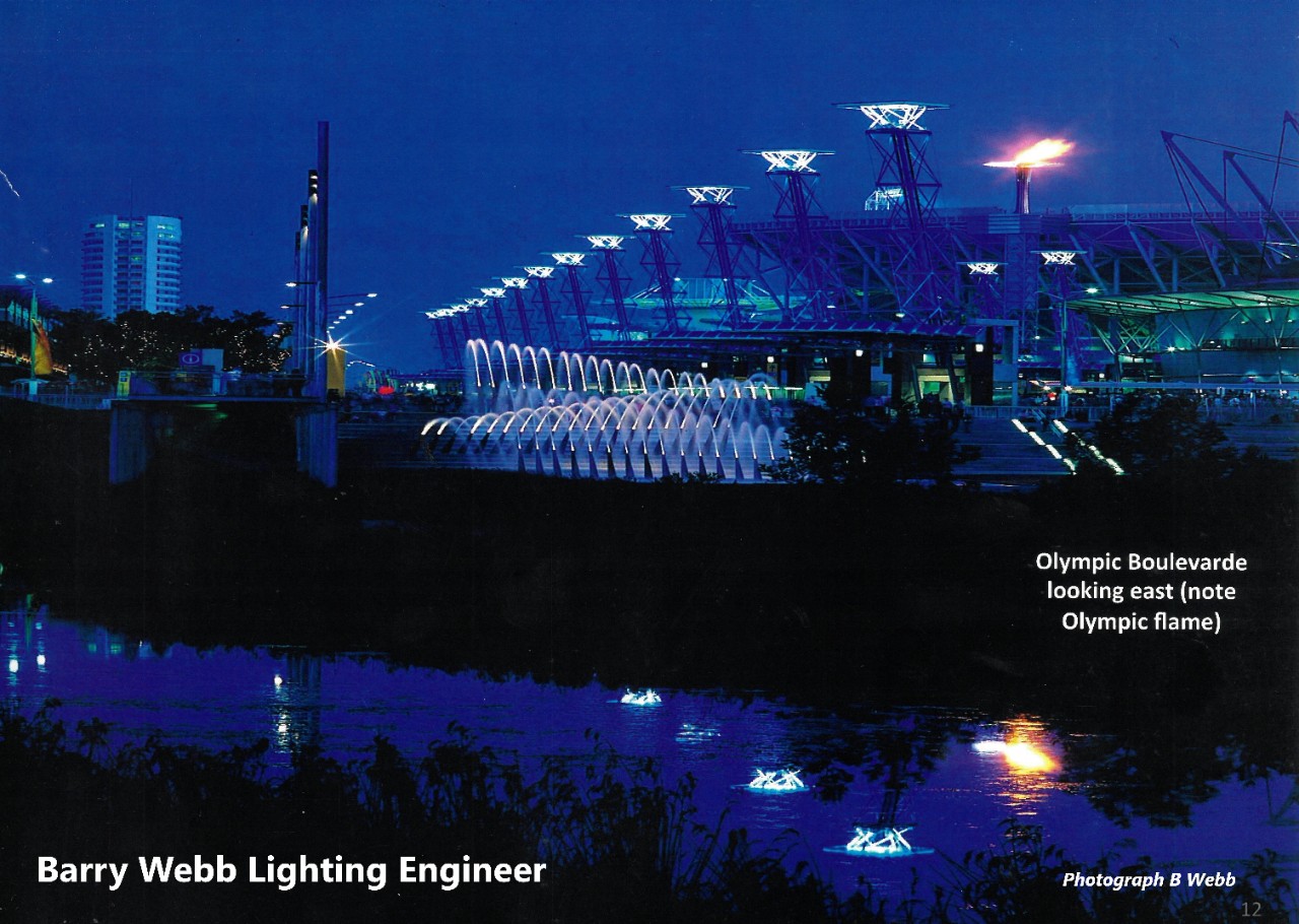 Olympic Boulevard illuminated at night during the Sydney Olympics. The Olympic torch burns above Barry Webb's solar-powered lighting design.